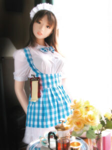 Orient Industry love doll in a blue gingham dress standing beside a tea set and flowers